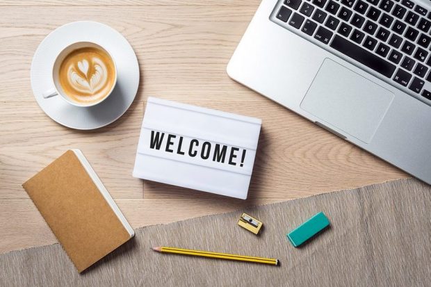 Welcome writing in lightbox lying on wooden desk with office supply and coffee cup as flat lay from bird's eye view