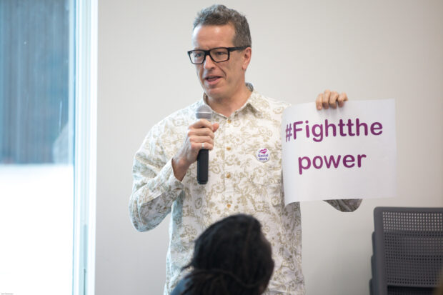 A man holds up a sign with the words fight the power on it as part of steering group discussions