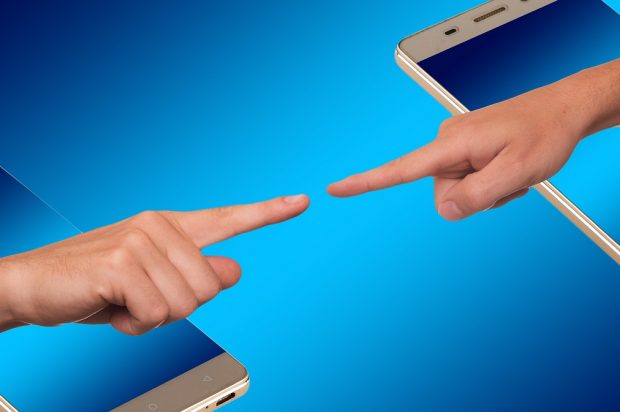 two hands reaching out of smartphones towards each other