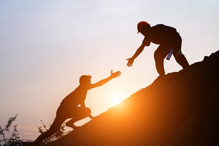 Man helping another man to go up the hill in the sunrise.