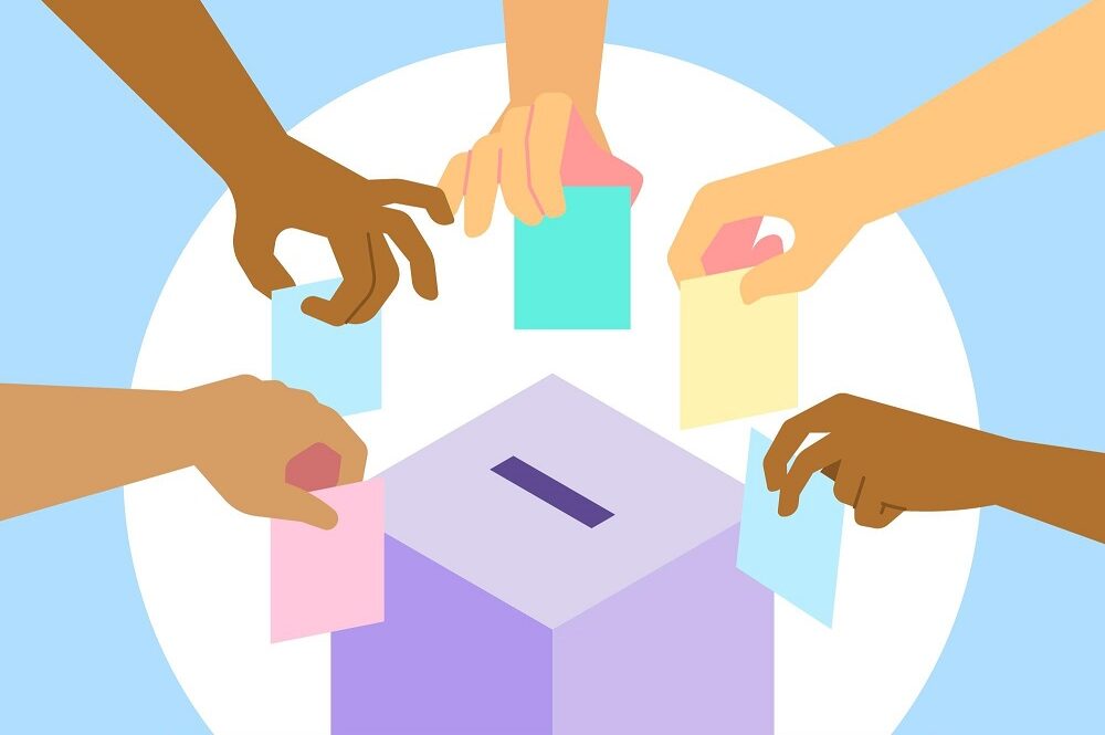 Hands of multiple ethnicities placing voting slips in a ballot box.